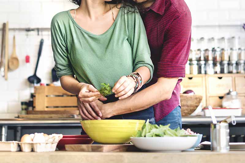 Horizontal image of a man hugging a woman as they make food.