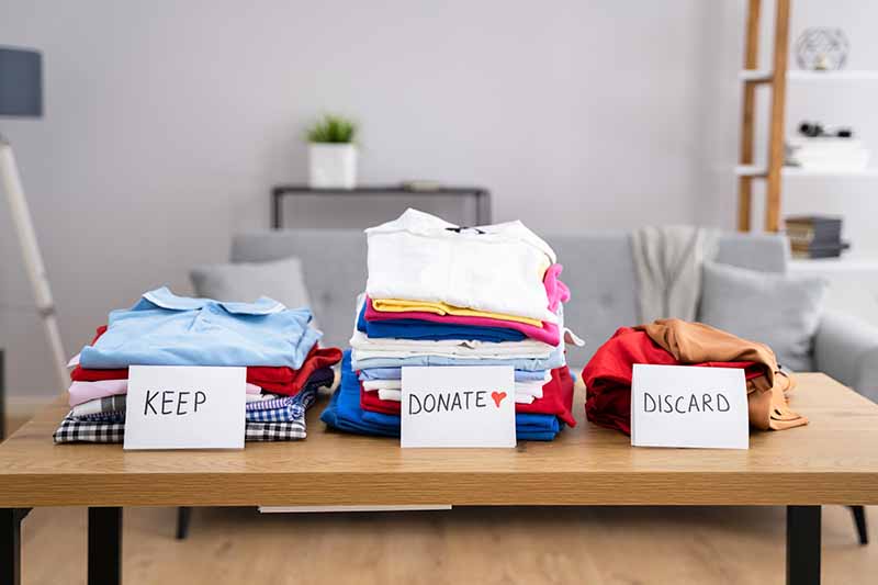 Horizontal image of piles of clothes to keep, donate, an discard on a table.