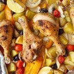 Horizontal image of cooked drumsticks on top of assorted vegetables on a foil-lined plate.