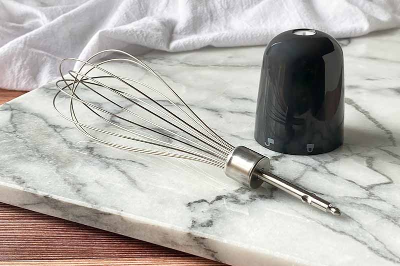 Horizontal image of a whisk and holder on a marble slab.
