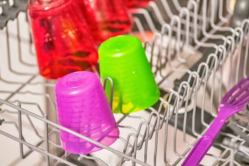 Horizontal image of colorful plastic cups and forks on a rack.