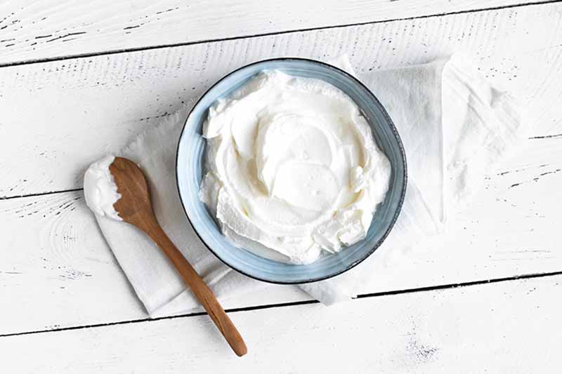 Horizontal image of a thick and spreadable white cream in a blue bowl next to a wooden spoon.