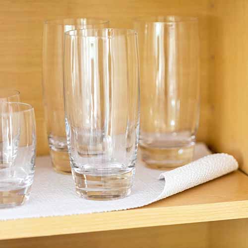 Image of empty glasses on top of a smooth top shelf liner in a cabinet.