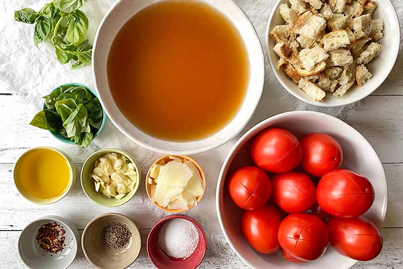 Horizontal image of assorted prepped and measured produce, seasonings, stock, and other ingredients in bowls.