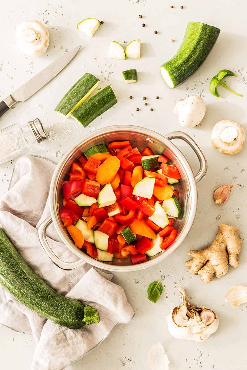 Vertical image of a pot filled with vegetables next to prepped ingredients and a knife.