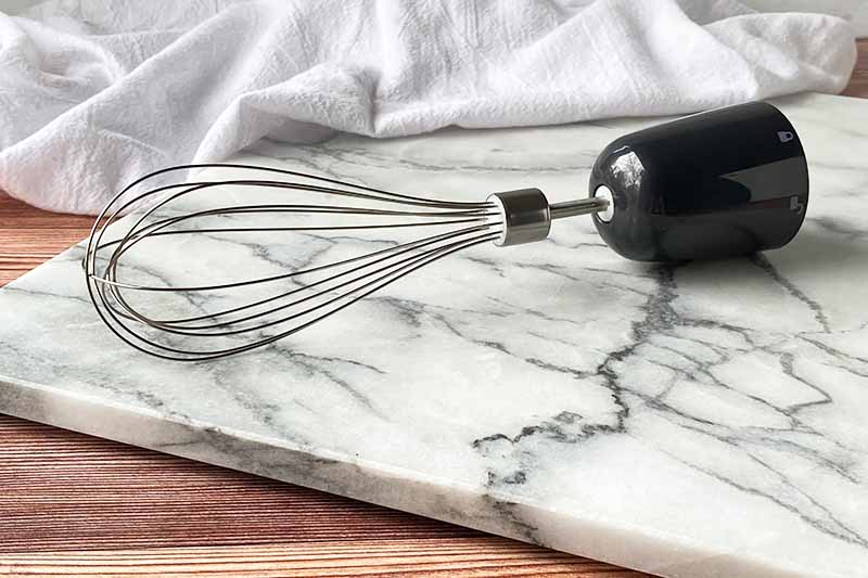 Horizontal image of a whisk and holder on a marble slab.