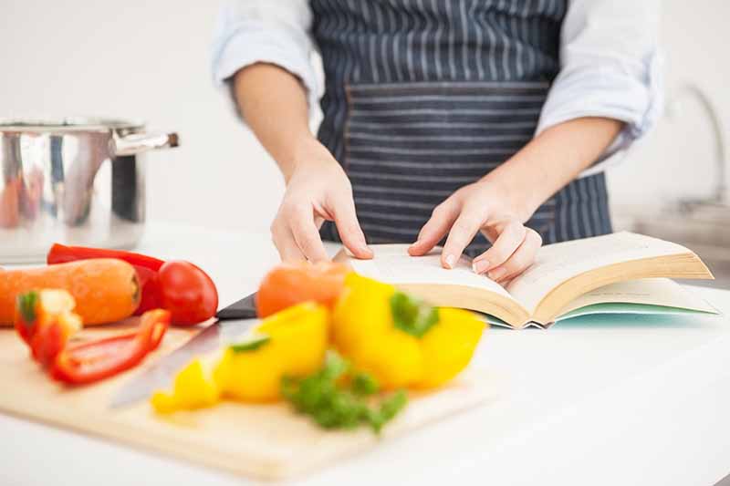 Horizontal image of reviewing a cookbook in on a countertop with fresh produce.
