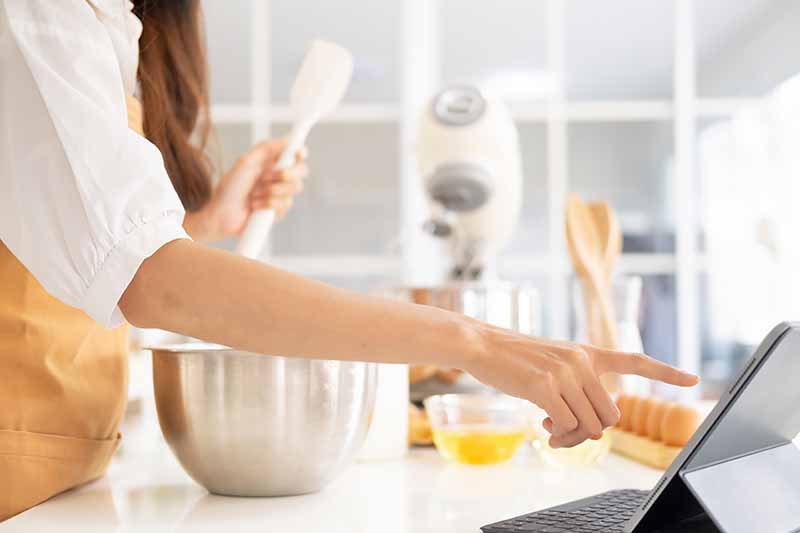 Horizontal image of a woman reviewing a cookbook while baking.