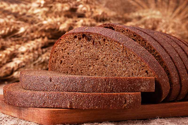 Horizontal image of a sliced loaf of rye bread on a wooden board.