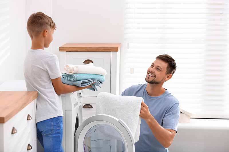Horizontal image of a man and son doing laundry together.