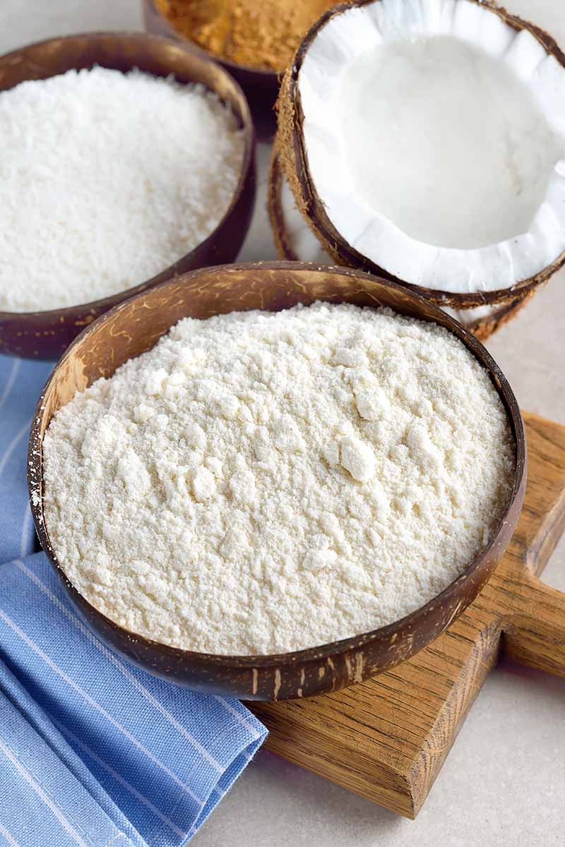 Vertical image of half of a whole coconut, coconut flakes, and coconut flour.