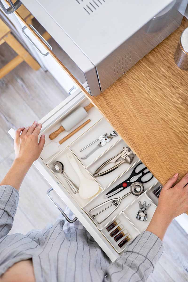 Vertical image of hands opening a small storage area with neatly arranged kitchen appliances.
