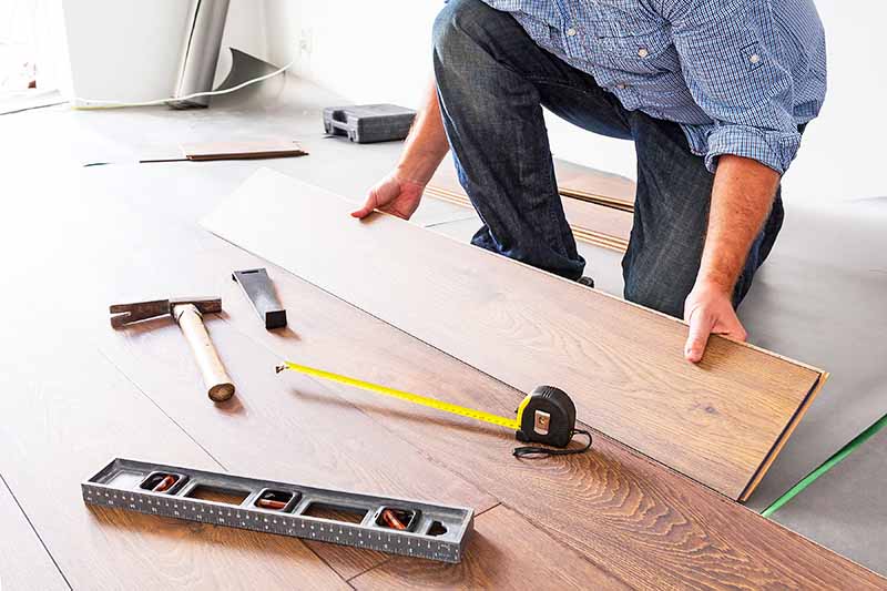 Horizontal image of a man installing new laminated wooden flooring.