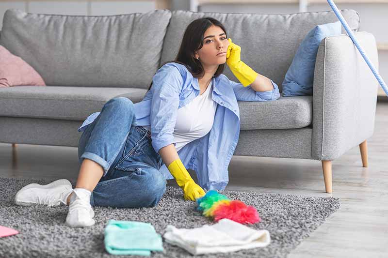 Horizontal image of a bored woman wearing yellow dish gloves on the floor of the living room.