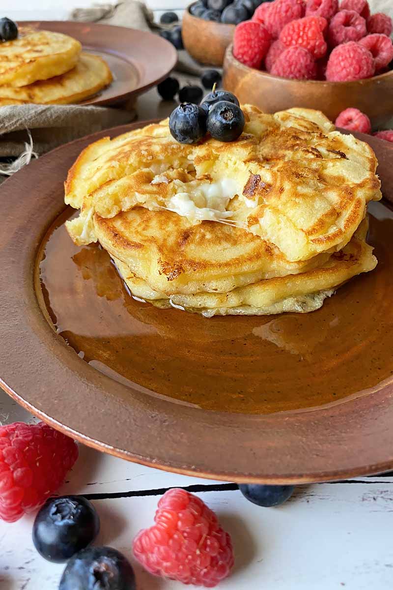 Vertical image of a torn pancake on a brown plate with maple syrup and fresh berries.