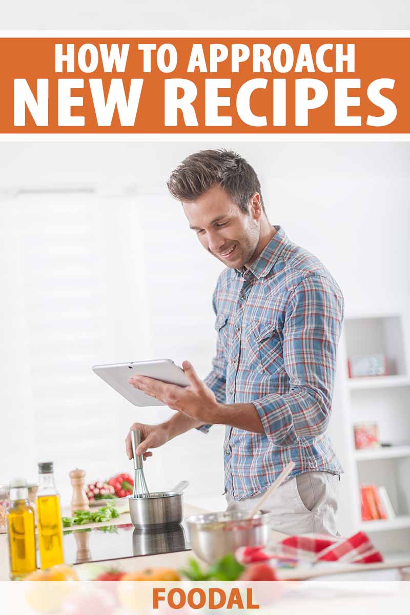 Image of a man preparing food in the kitchen while reading his tablet.