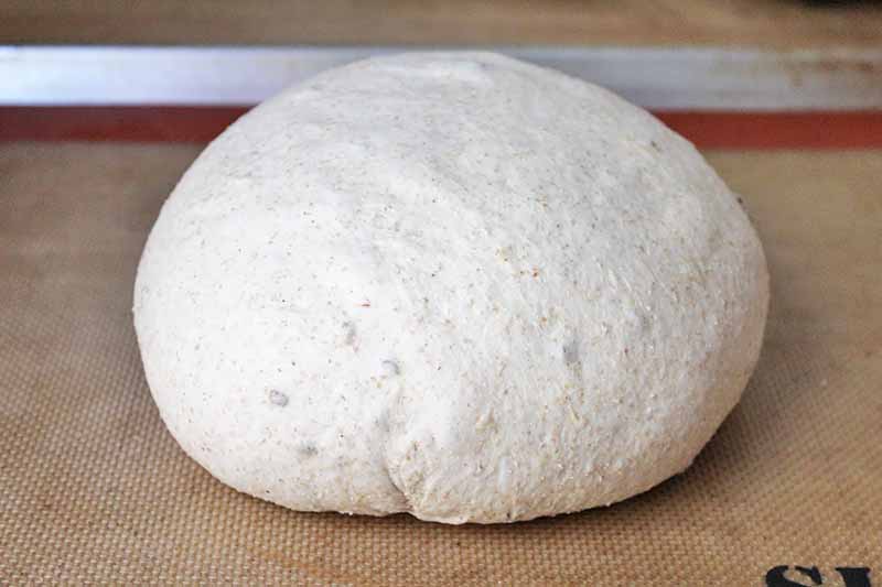 Horizontal image of an unbaked round of bread on a Silpat-lined baking sheet.