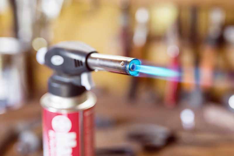 Horizontal image of a gas cartridge and lighter with a blue flame.