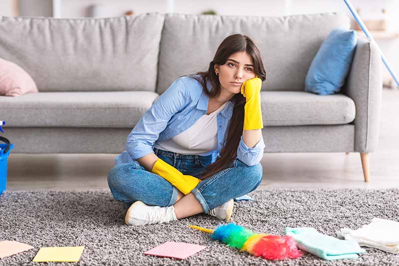 Horizontal image of a bored woman wearing yellow dish gloves on the floor of the living room.
