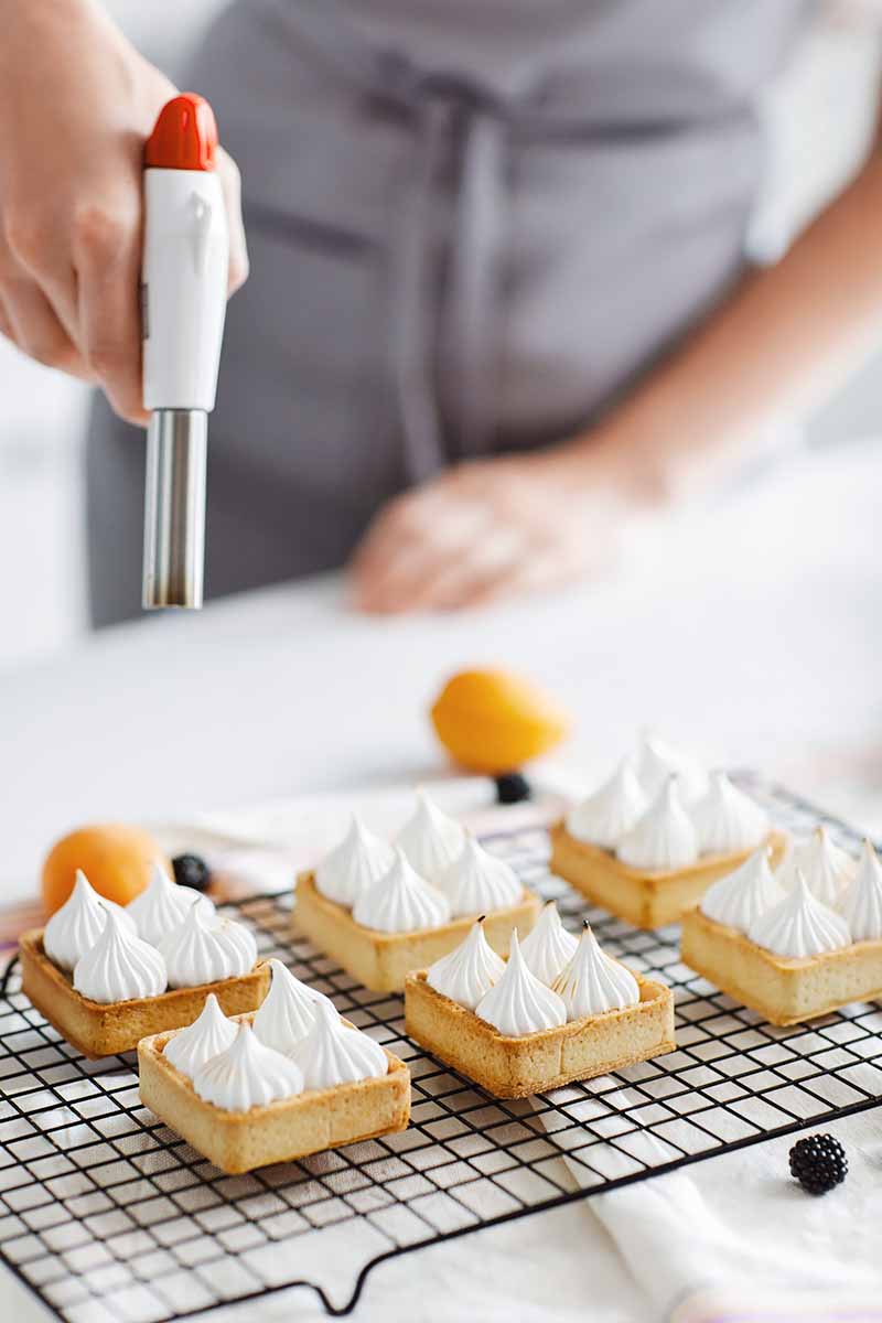 Vertical image of a cook browning the meringue on the top of tarts.