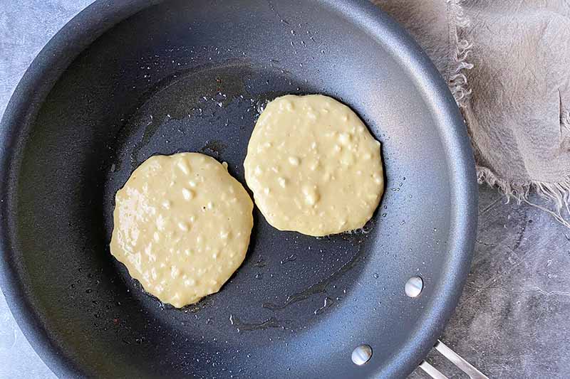 Horizontal image of cooking two small flapjacks in a greased skillet.