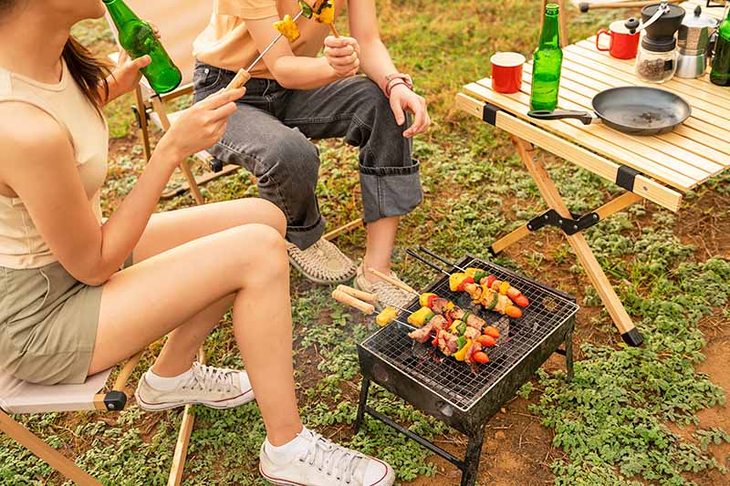 Horizontal image of a couple preparing kebabs on a barbecue outdoors.