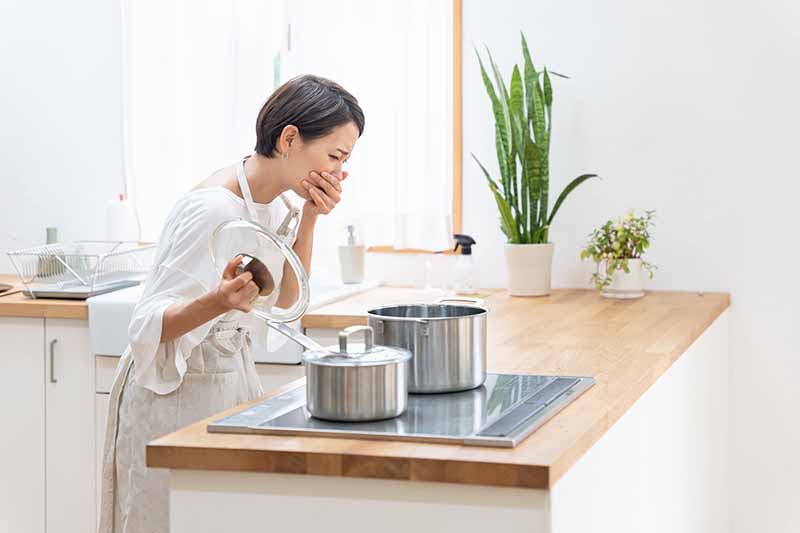 Horizontal image of a woman making a mistake while preparing food in pots.