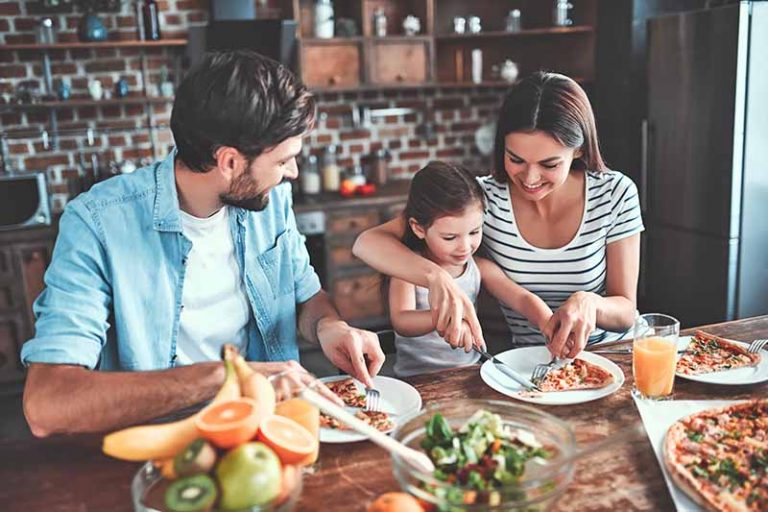 Horizontal image of a mom, dad, and daughter enjoying pizza together at the table.