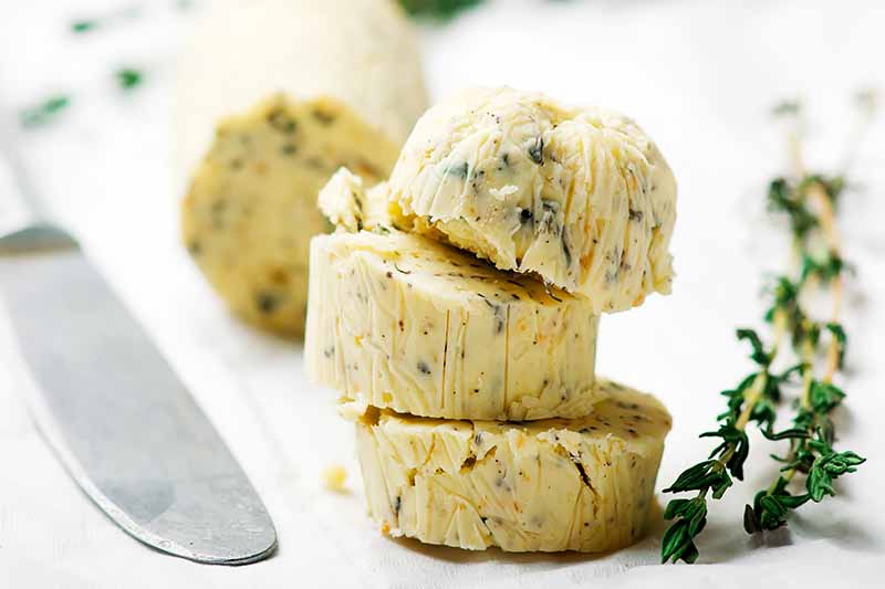 Horizontal image of sliced of compound butter next to fresh thyme.