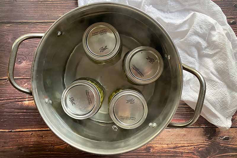 Horizontal image of water bath canning four glass jars.