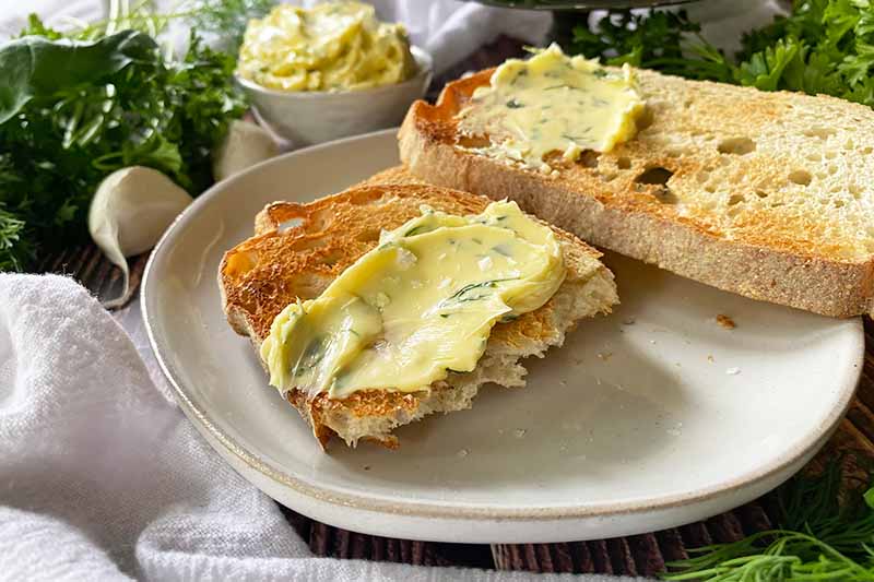 Horizontal image of slices of toasted bread spread with a yellow condiment mixed with finely chopped greens on a white plate.