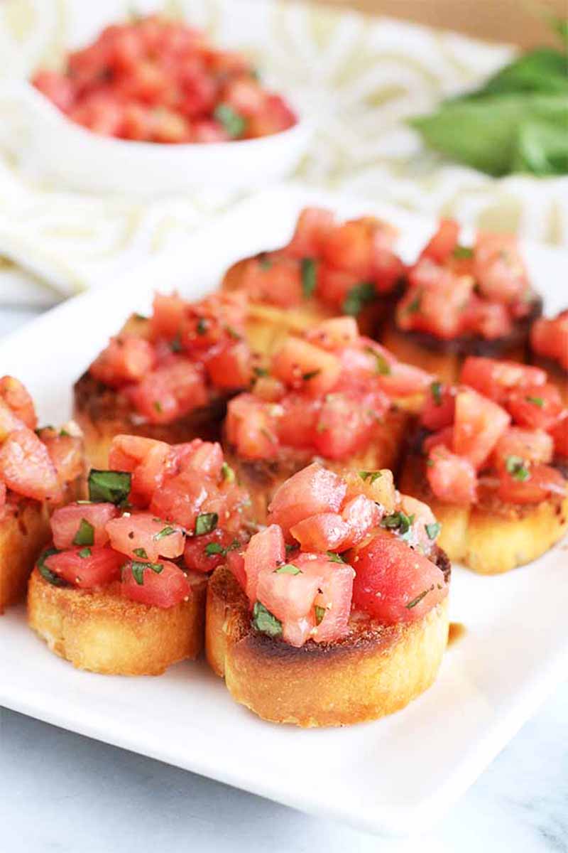 Vertical image of a white plate with bruschetta topped with chopped tomatoes and herbs.