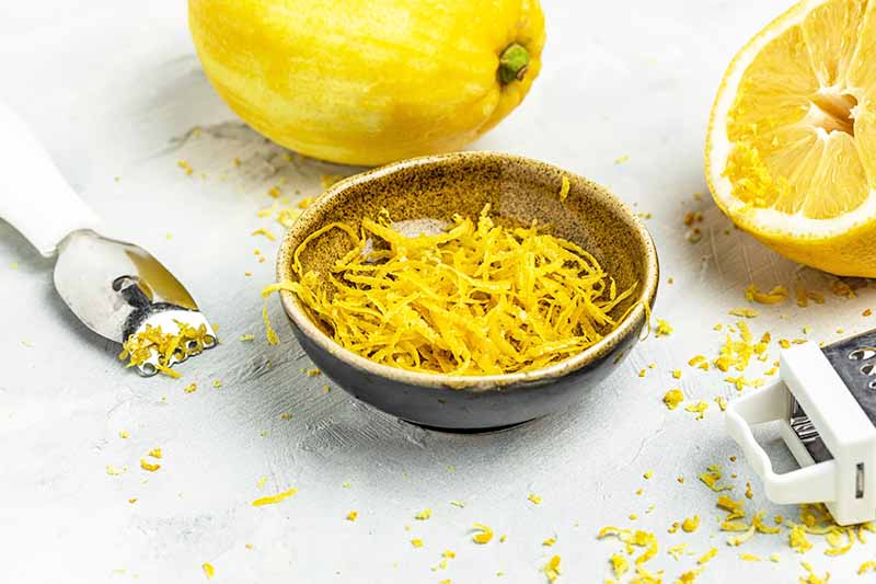 Horizontal image of lemon zest in a bowl next to a whole lemon and a grater.