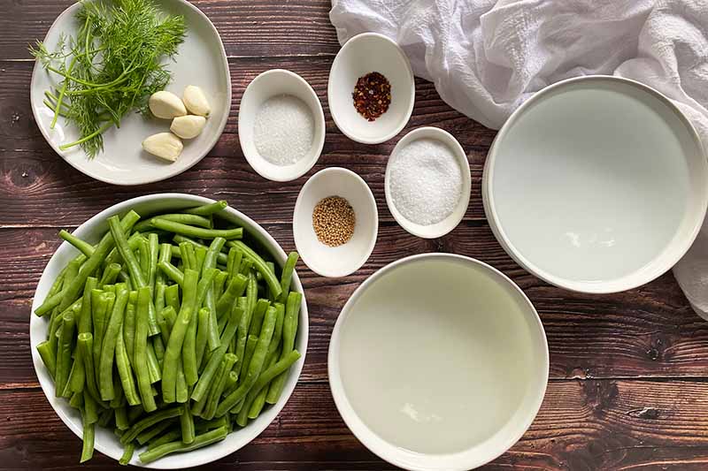 Horizontal image of assorted ingredients for canning vegetables in white bowls and plates.