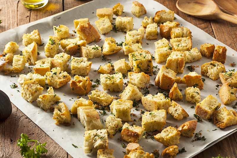 Horizontal image of toasted croutons with herbs on a baking sheet.