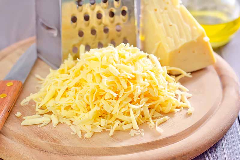 Horizontal image of shredded cheese on a wooden block next to a grater.