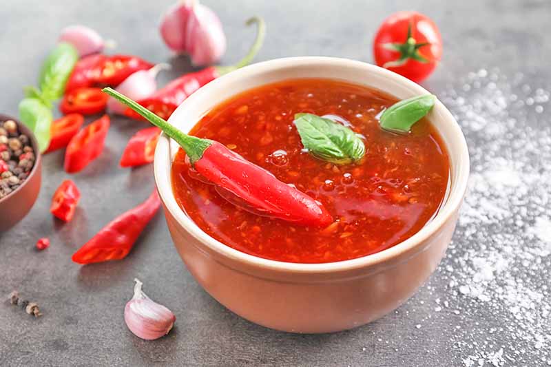 Horizontal image of a spicy red sauce in a bowl on a table next to peppers.