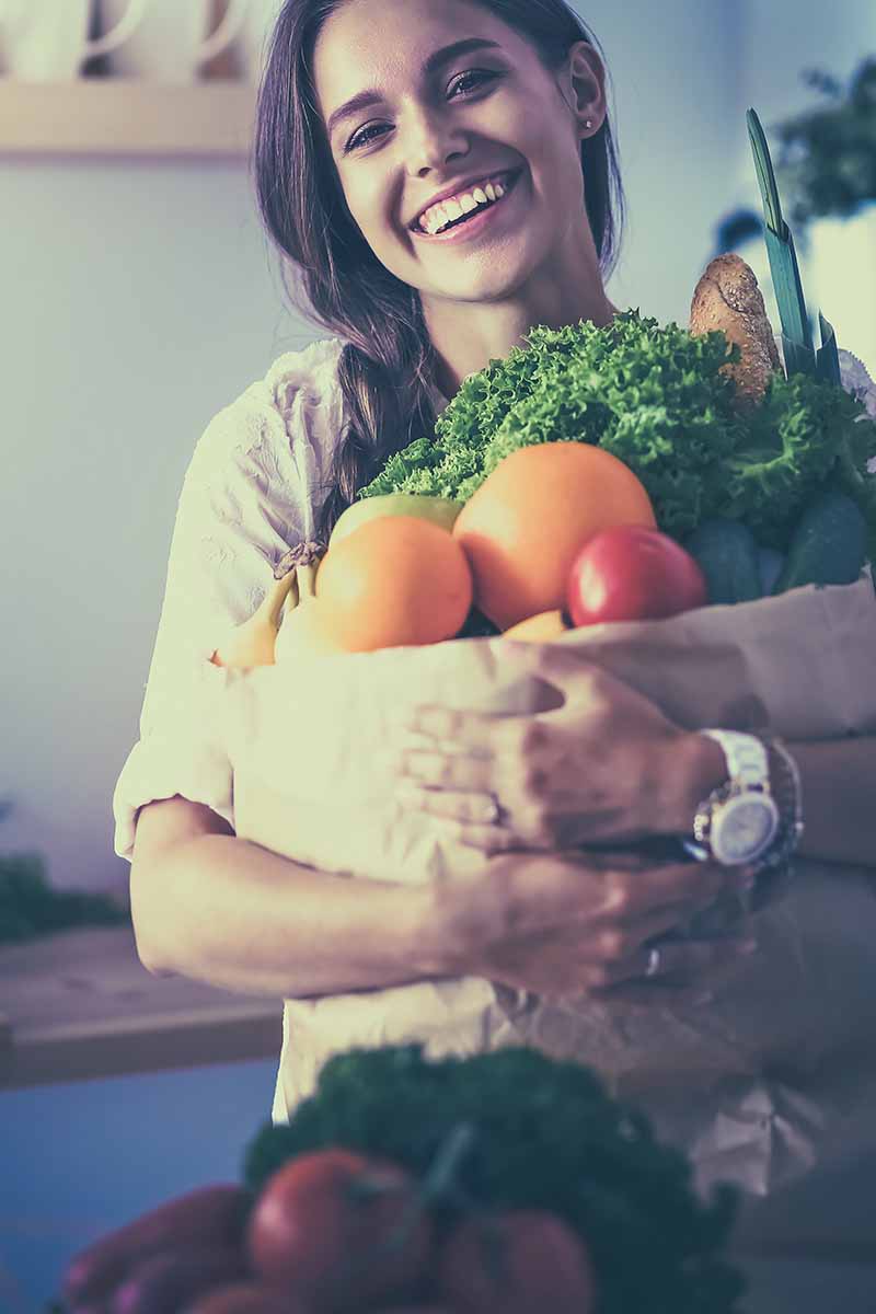 Vertical image of a woman holding a paper bag full of groceries.
