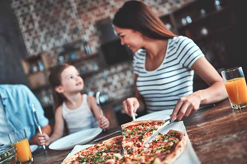 Horizontal image of a woman serving pizza to her family at the table.