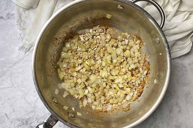 Horizontal image of cooking diced onions and garlic in a pot.