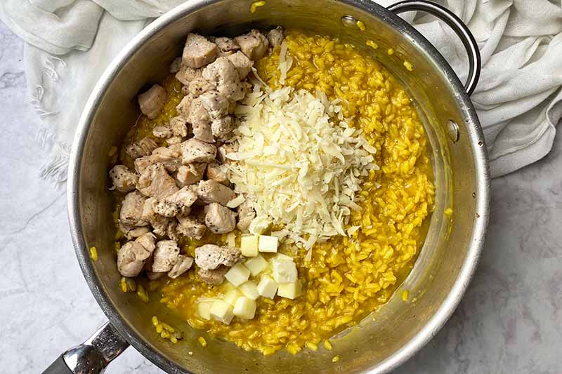 Horizontal image of a pile of cooked meat, a pile of shredded cheese, and a pile of cubed butter on top of a yellow-tinted stew.