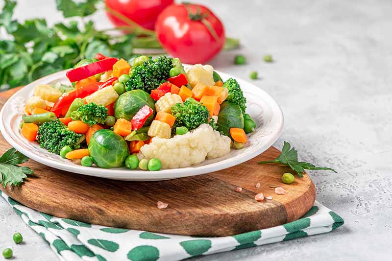Horizontal image of a plateful of cooked plain cauliflower, brussels sprouts, peas, broccoli, and peppers.