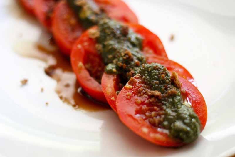 Horizontal image of slices of ripe tomatoes topped with a green herb sauce.