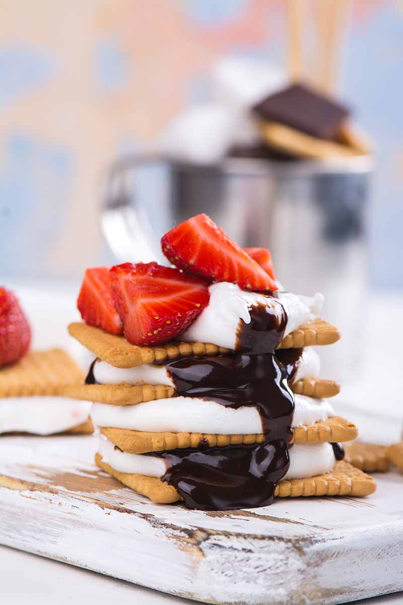 Vertical image of a stack of cookies, marshmallows, and ganache on a white board.