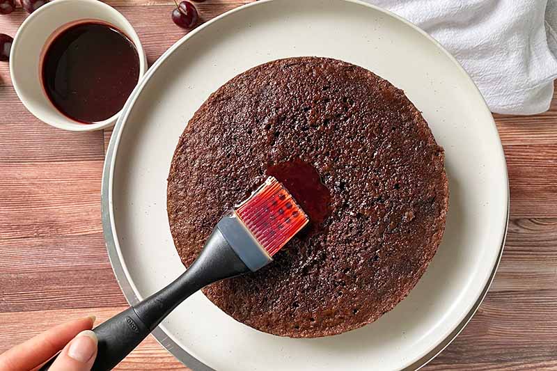 Horizontal image of brushing the top of a cake with a syrup.