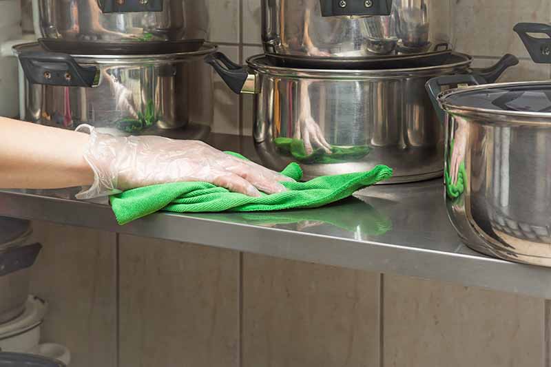 Horizontal image of a gloved hand holding a rag over a counter surface.