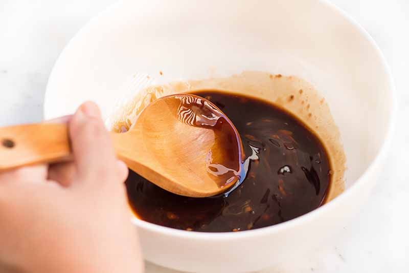 Horizontal image of mixing together a dark sauce in a white bowl.
