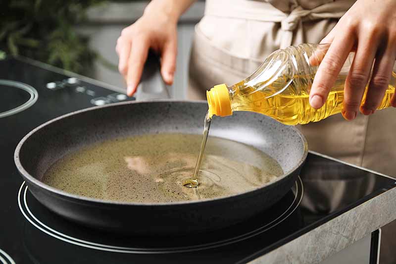 Horizontal image of pouring vegetable oil into a shallow pan in the kitchen.