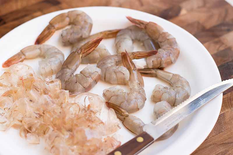 Horizontal image of peeling raw small prawns on a plate.
