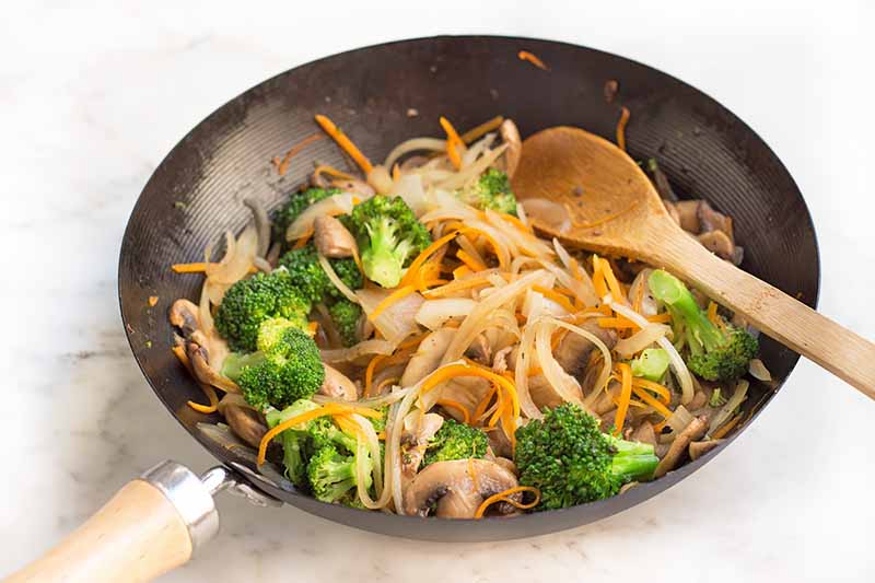 Horizontal image of cooking assorted vegetables in a wok.